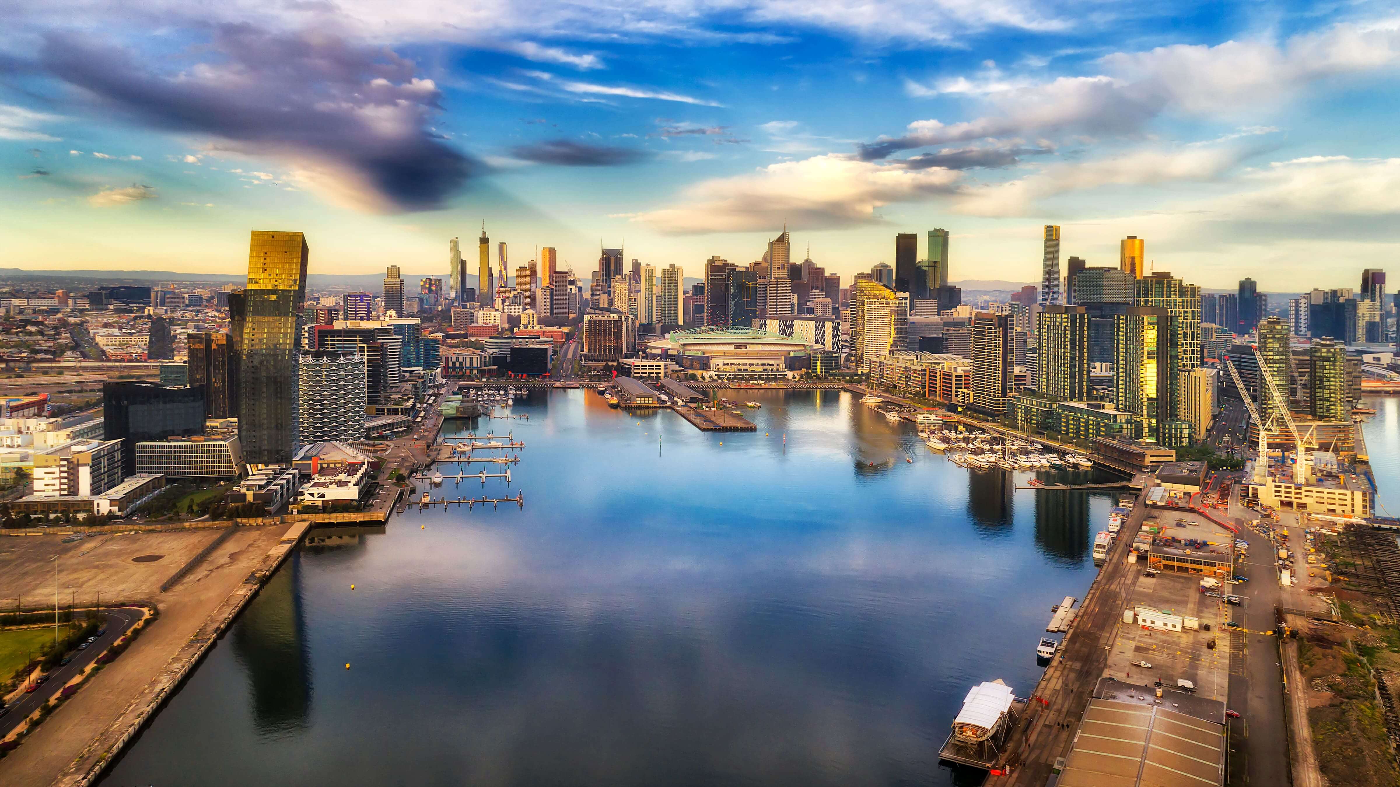 Yarra river surrounded by Melbourne suburb Docklands in elevated aerial view facing city CBD waterfront and towers with marina and yachts.